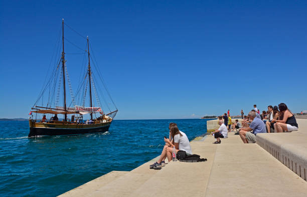 Zadar, Croatia - June 18th 2016. Tourists watch the boats go by as they listen to the Sea Organ (Morske Orgulje) on zadar's waterfont. This experimental musical instrument plays music through the movement of sea waves and tubes positioned under the steps.